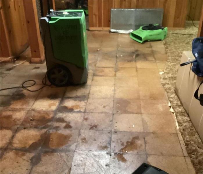Basement tile floor with green SERVPRO drying equipment and partially removed carpeting visible