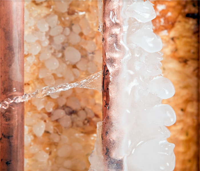 a frozen copper pipe with icicles on one side and water leaking from the other